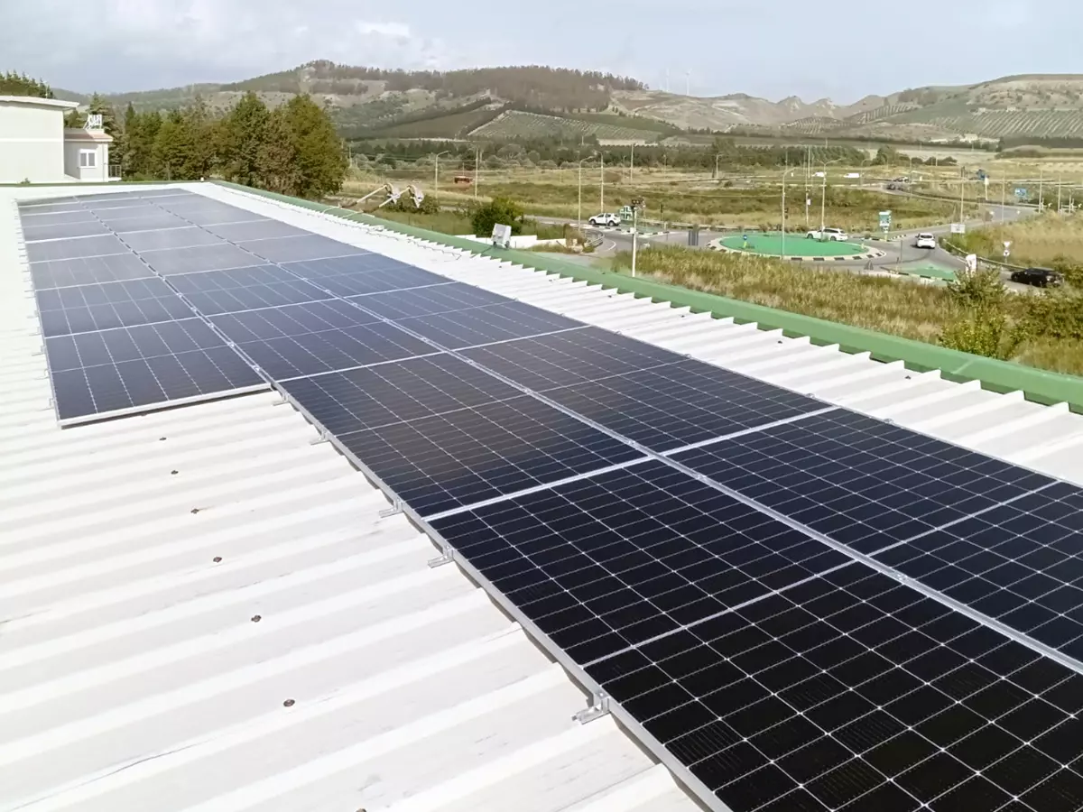 Pannelli fotovoltaici da 15 kW installati sul tetto in lamiera di un'azienda a Catanzaro, con colline e una rotonda sullo sfondo.